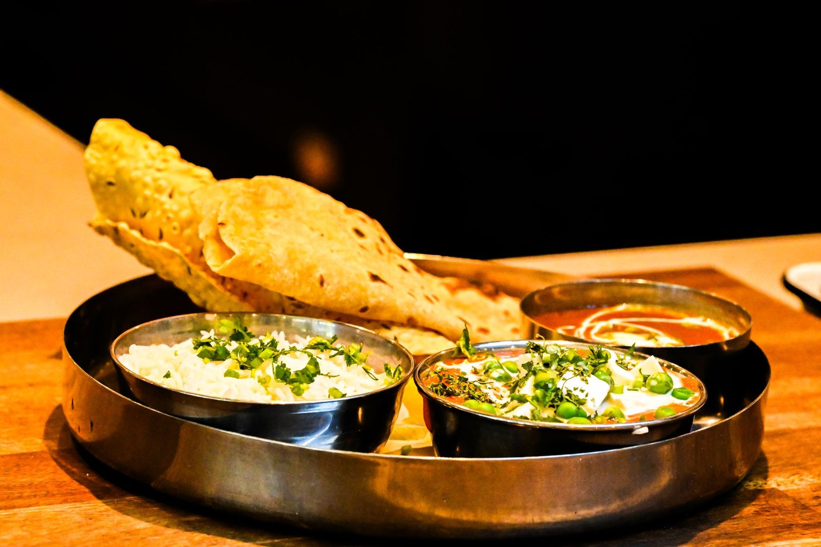 Traditional Indian thali with naan, paneer curry and rice on a wooden table, fresh food served safely