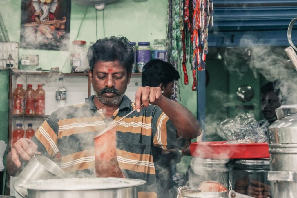 Vendor making traditional masala chai surrounded by steam at an Indian tea stall during the rainy season