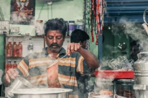 Vendor making traditional masala chai surrounded by steam at an Indian tea stall during the rainy season