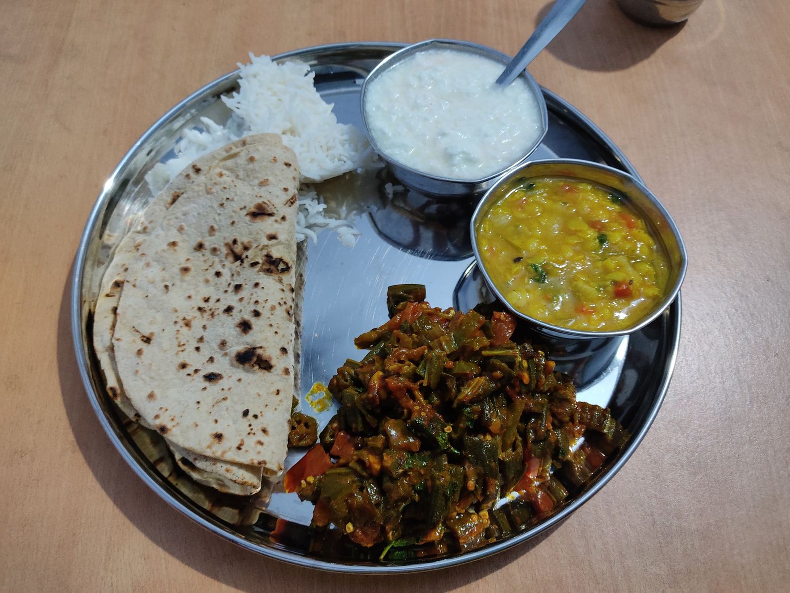 Traditional Indian vegetarian thali with chapati, rice, dal, okra and yogurt on a plate