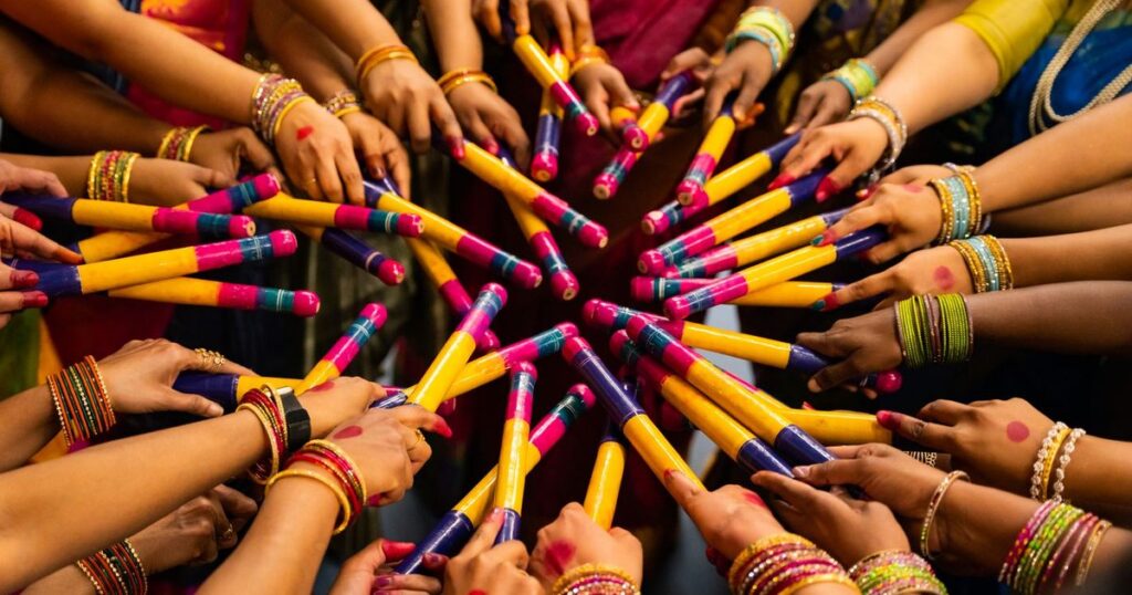 Women in colourful saris and glass bangles holding painted dandiya sticks in a circle during a Navratri garba night