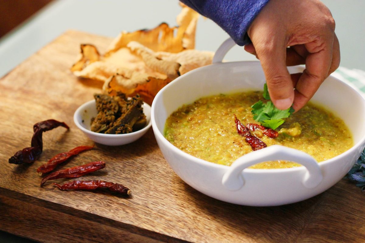 Bowl of yellow khichdi garnished with fresh coriander and dried red chilli, served with papad as a light vrat-style meal