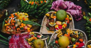 Bamboo soop baskets of Chhath prasad on the ground: thekua, gagal lemon, bananas, apples, radish, sugarcane and marigolds, with lit diyas