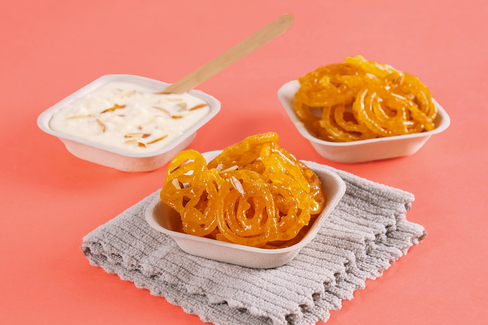 Jalebi in two CHUK bagasse donas next to a dona of rabri with almond slivers and a wooden spoon